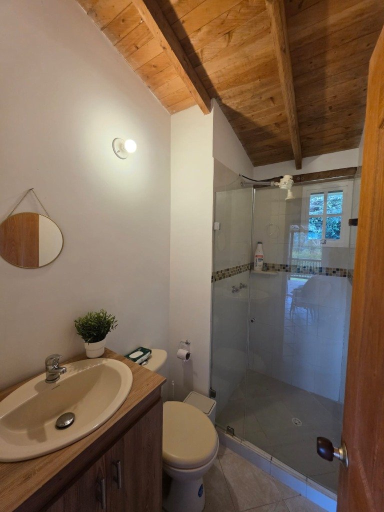 Baño completo moderno con ducha en cabina de vidrio templado, lavamanos y espejo en Casa Campestre La Isabela