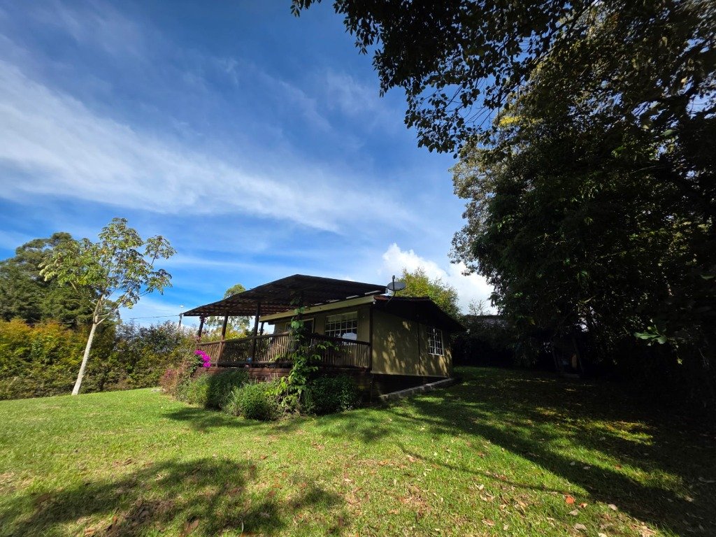 Fotografía real de la fachada principal de Casa Campestre La Isabela con pórtico de madera, flores y prados en Las Lomitas, La Ceja